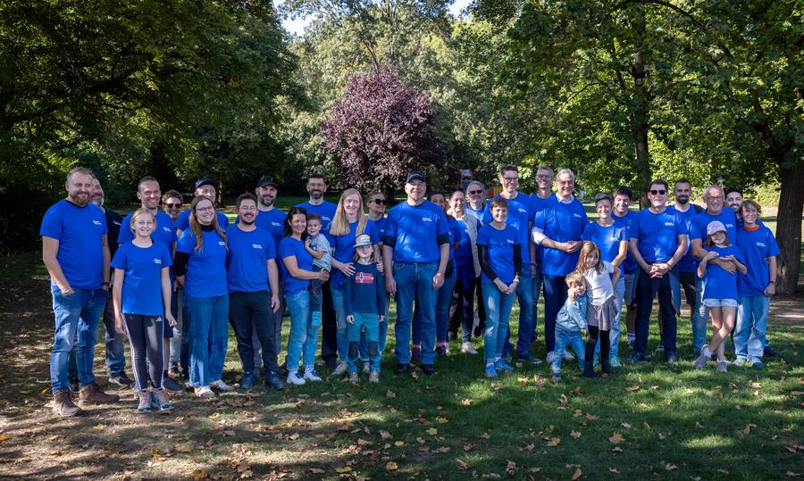Große Gruppe von Erwachsenen und Kindern bei einer gemeinsamen Aktion in einer Grünanlage.