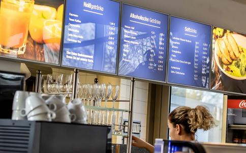 Digitale Getränkekarte in einem Café zeigt Preise für Heißgetränke, alkoholische Getränke und Softdrinks über der Theke