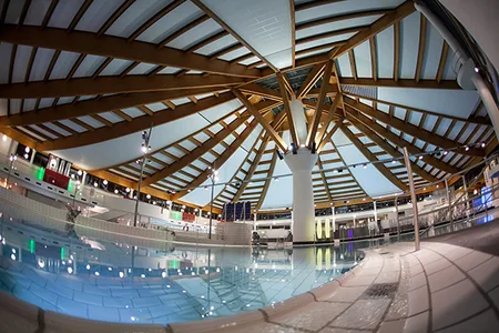Innenansicht eines Schwimmbads mit großem Becken und sichtbarer Holztragkonstruktion an der Decke