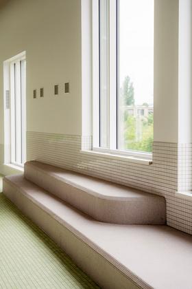 Innenraum mit großen Fenstern und einer mehrstufigen Sitzbank mit kleinen quadratischen Fliesen an Wand und Sitzfläche
