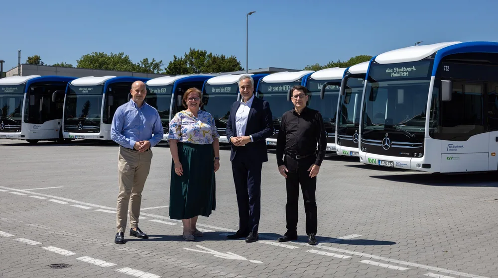 Vier Personen stehen auf dem Betriebshof vor einer Reihe moderner weiß-blauer Elektrobusse von das Stadtwerk.Mobilität. Die Fahrzeuge sind nebeneinander aufgestellt.