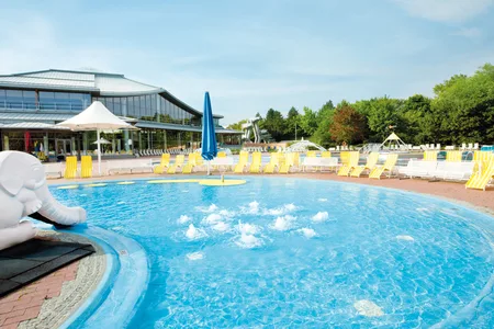 Außenbecken mit Wassersprudlern und gelben Liegestühlen im Freibad Westbad, modernes gläsernes Gebäude im Hintergrund