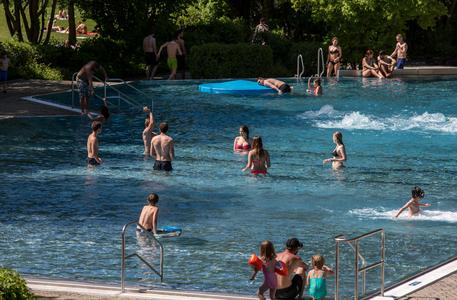 Mehrere Menschen unterschiedlichen Alters schwimmen und spielen in einem Freibad bei Sonnenschein