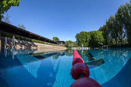 Freiluft-Schwimmbecken mit klar blauem Wasser, Schwimmbahnmarkierungen und umgebenden Bäumen unter klarem Himmel