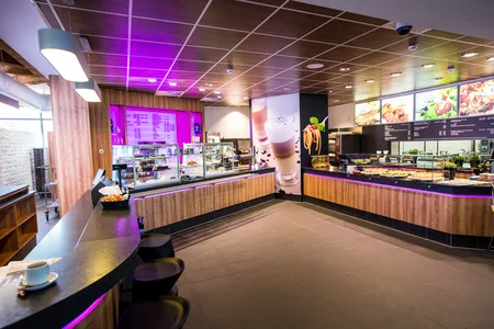 Innenansicht eines modernen Cafés mit Theken, Sitzplätzen und beleuchteten Speisekarten an der Wand