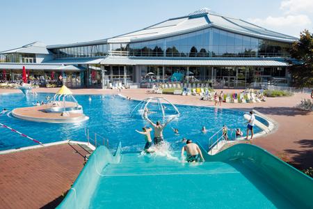 Kinder rutschen eine Wasserrutsche im Außenbecken des Westbads, im Hintergrund modernes Schwimmbadgebäude mit großen Glasfenstern