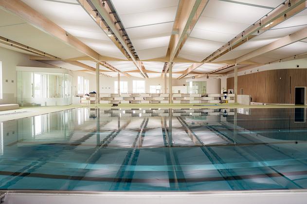 Innenansicht eines großen Hallenbads mit Schwimmbecken und Holzdeckenbalken