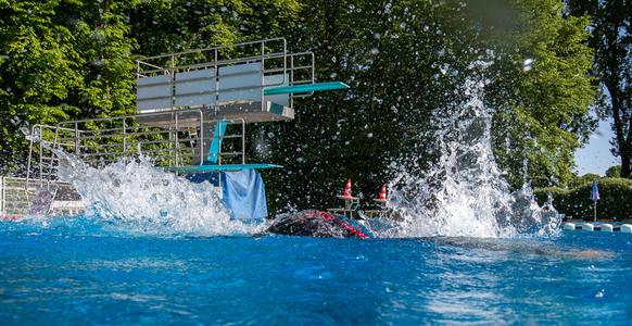 Springturm mit mehreren Plattformen über einem Schwimmbecken, Wasser spritzt nach einem Sprung