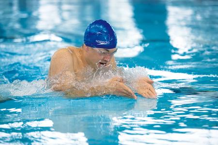 Schwimmer mit blauer Badekappe führt Brustschwimmzug im Hallenbad aus
