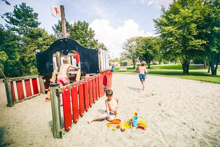 Kinder spielen an einem roten und schwarzen Piratenschiff-Spielplatz aus Holz im Sand unter Bäumen