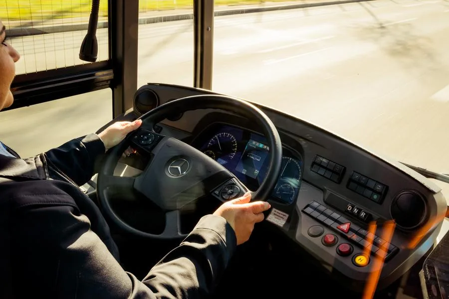  Eine Person sitzt am Steuer eines Linienbusses, hält mit beiden Händen das Lenkrad und blickt nach vorne. 