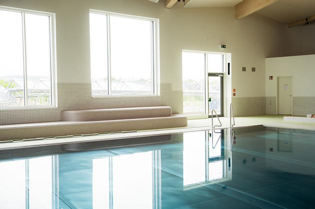 Innenansicht eines Schwimmbads mit großem Fenster, Sitzbank und ruhiger Wasseroberfläche