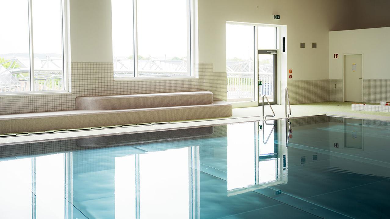 Innenansicht eines Schwimmbads mit großem Fenster, Sitzbank und ruhiger Wasseroberfläche