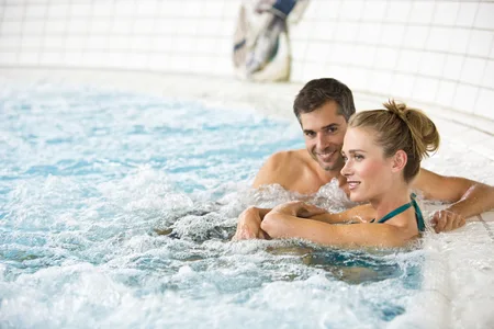 Zwei Personen entspannen im Whirlpool eines Hallenbads mit weißen Fliesenwänden