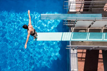 Mann steht auf dem Sprungbrett vor seinem Sprung in ein Schwimmbecken mit klarem Wasser